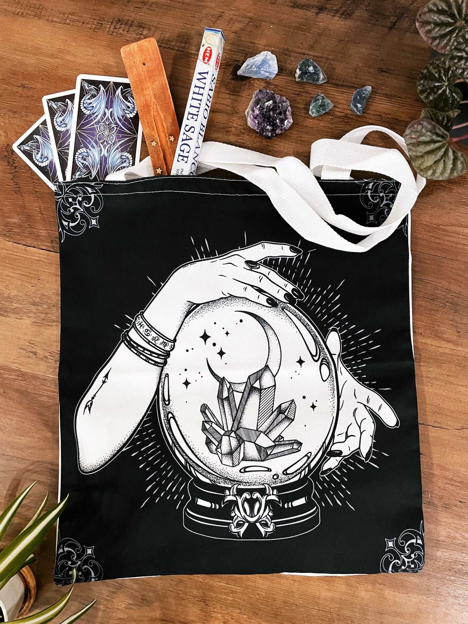 Pictured is a large canvas tote bag featuring an image of two hands around a crystal ball with crystals inside. Black Crystal Ball & Crystals Tote Bag