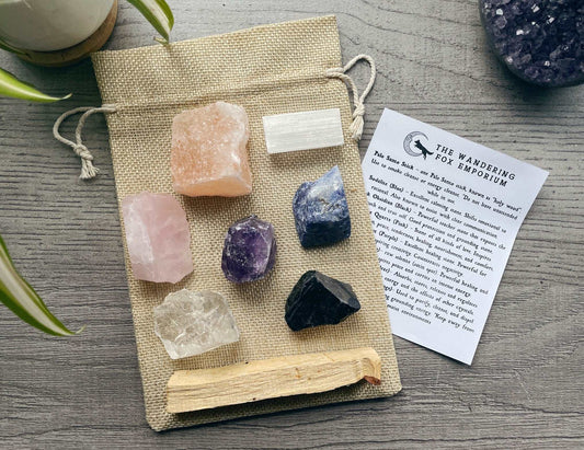 Pictured is a crystal starter set with various raw crystals and a palo santo stick. A piece of paper is nearby with the information about the crystals on it. Crystal Starter Set