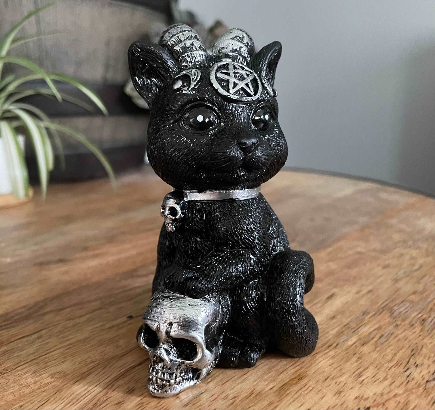 Pictured is a resin statue of a black cat with horns and a pentagram on its forehead with a paw on a silver skull. Demon Cat Figurine side