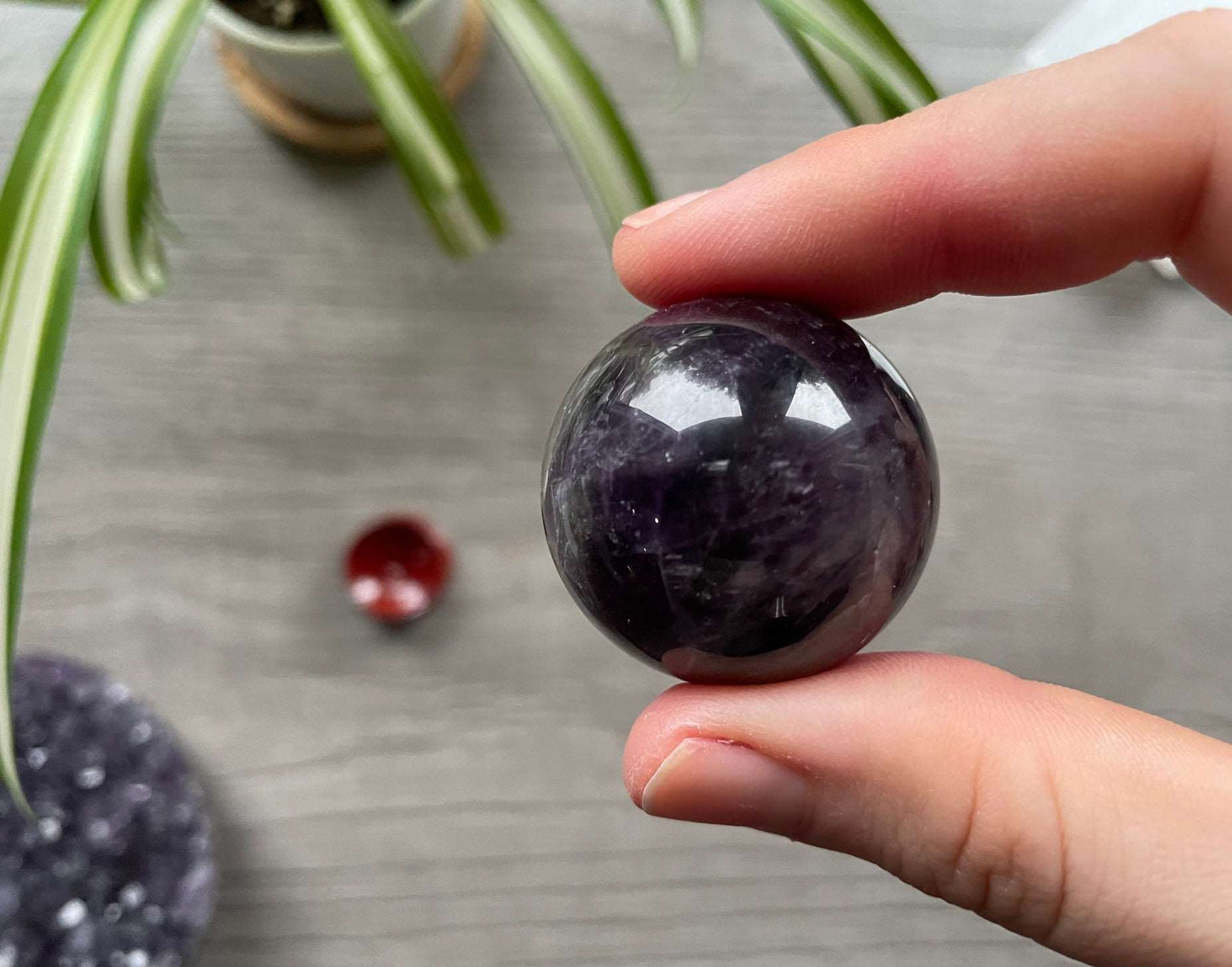 A polished sphere of amethyst is shown in the image. The crystal is a purple color and has a smooth, shiny surface. Amethyst Crystal Sphere 33mm