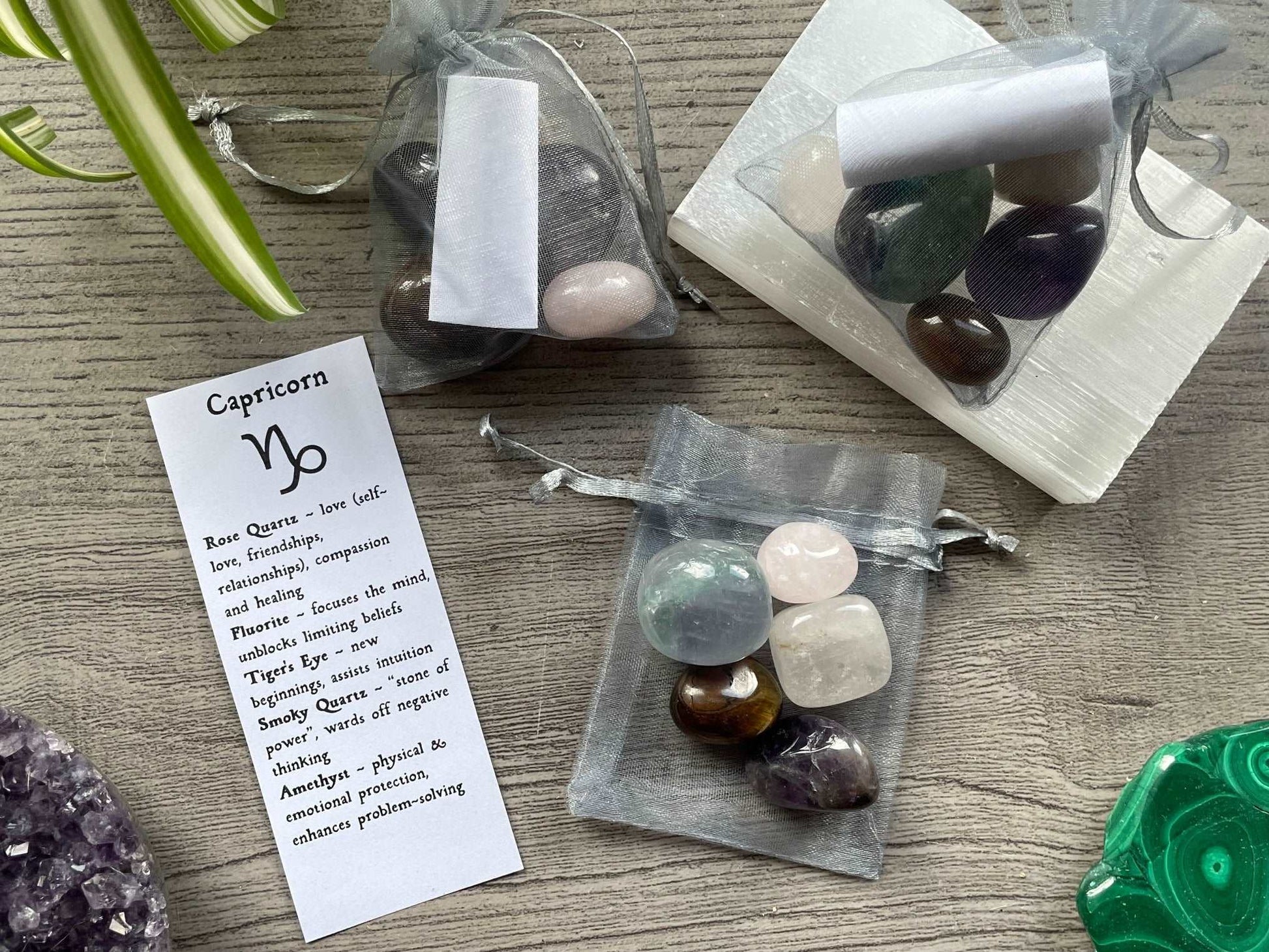 An image of a collection of tumbled stones in an organza bag. To the side is a piece of paper that describes what each tumbled stone's metaphysical properties are. CAPRICORN Zodiac Tumbled Crystal Bag