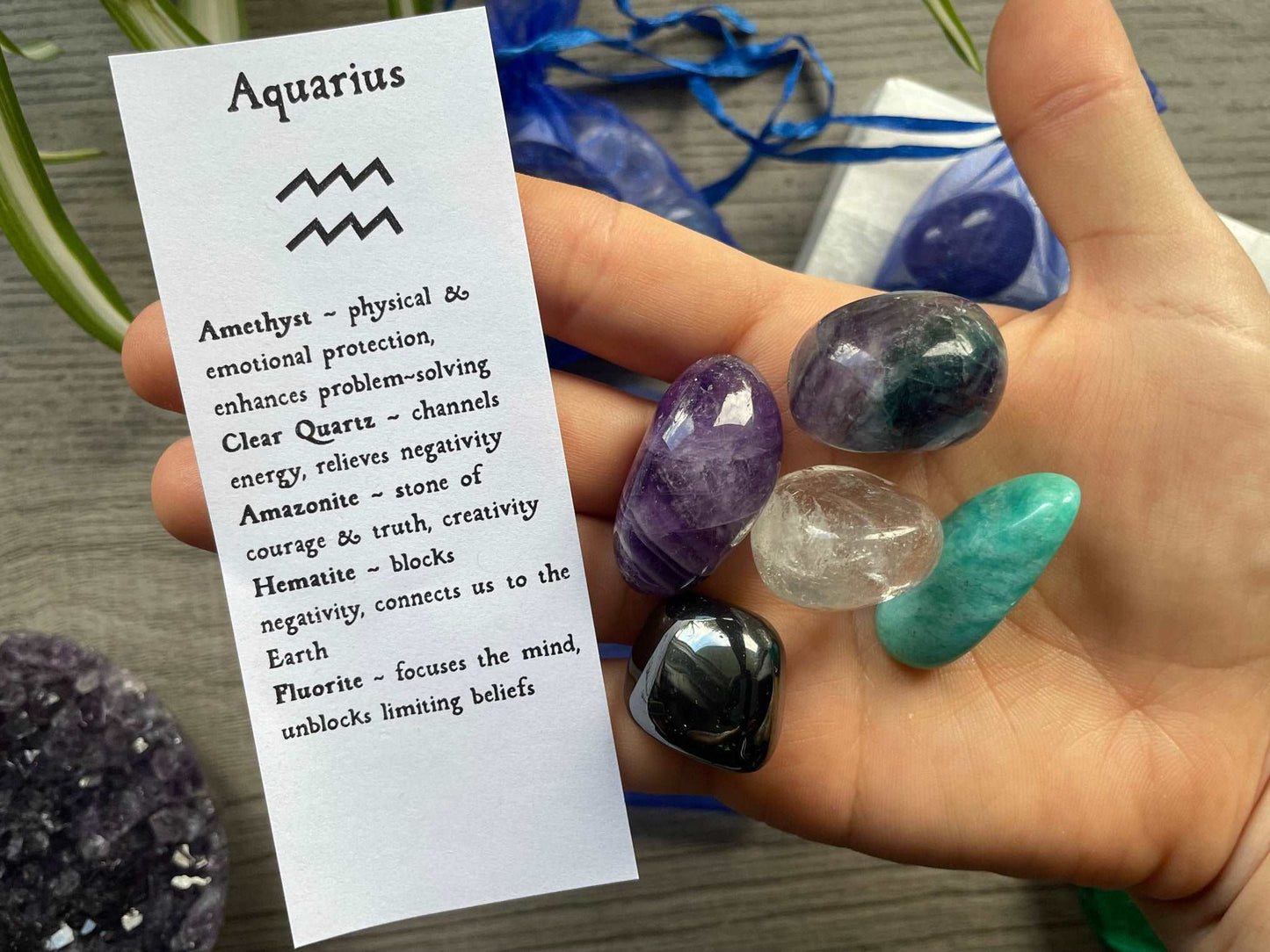 An image of a collection of tumbled stones in an organza bag. To the side is a piece of paper that describes what each tumbled stone's metaphysical properties are. AQUARIUS Zodiac Tumbled Crystal Bag crystals