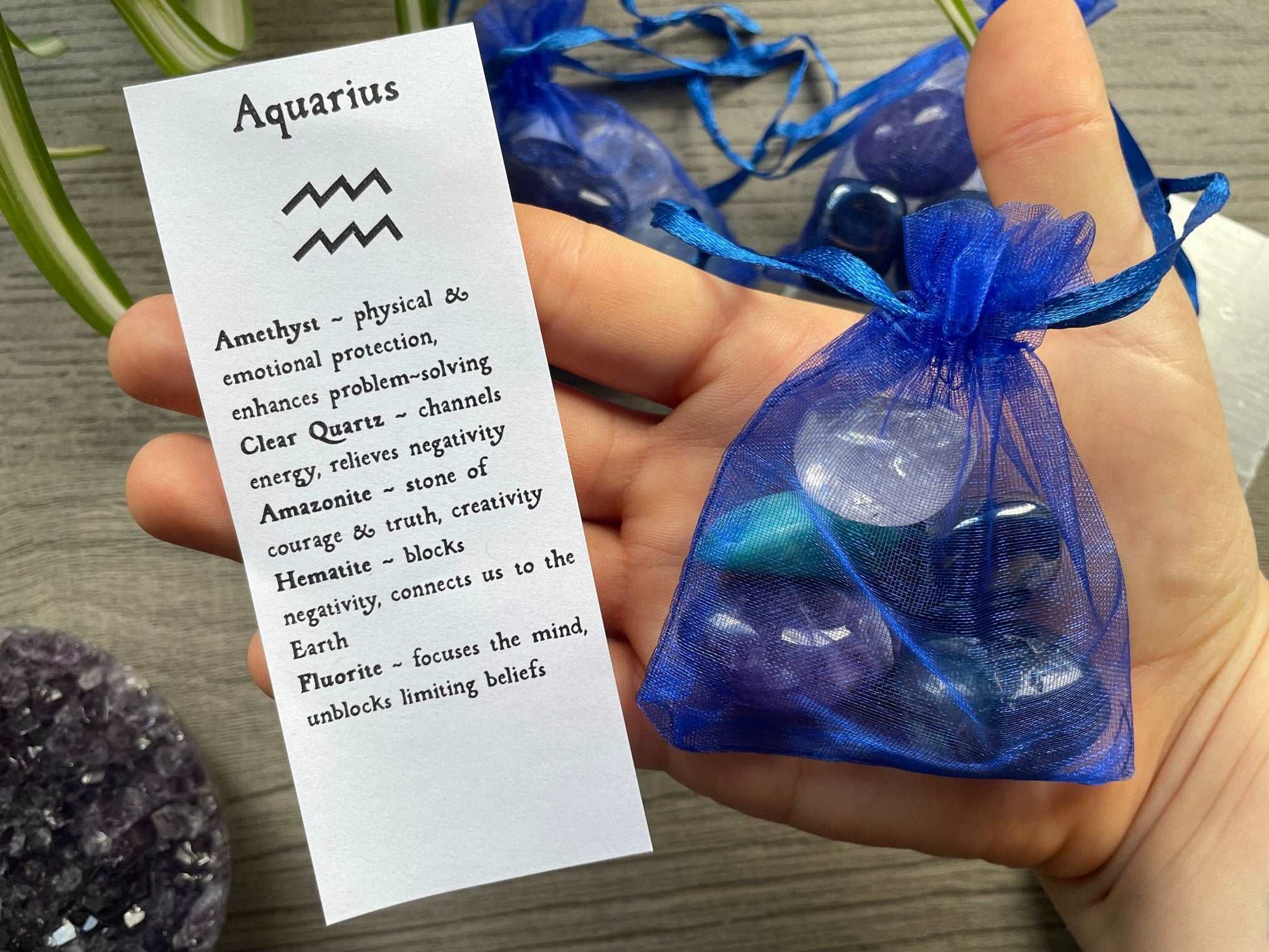 An image of a collection of tumbled stones in an organza bag. To the side is a piece of paper that describes what each tumbled stone's metaphysical properties are. AQUARIUS Zodiac Tumbled Crystal Bag close up