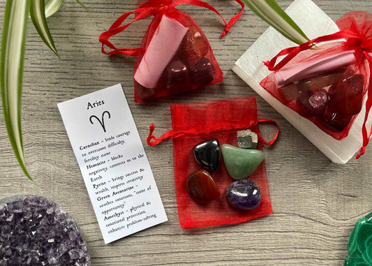 An image of a collection of tumbled stones in an organza bag. To the side is a piece of paper that describes what each tumbled stone's metaphysical properties are. ARIES Zodiac Tumbled Crystal Bag