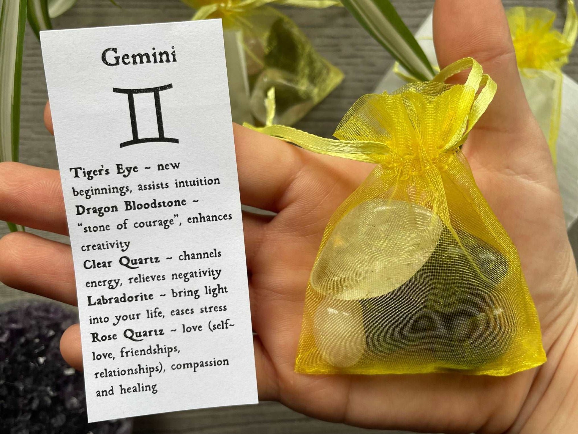 An image of a collection of tumbled stones in an organza bag. To the side is a piece of paper that describes what each tumbled stone's metaphysical properties are. GEMINI Zodiac Tumbled Crystal Bag close up