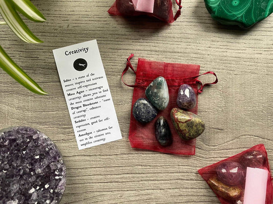 An image of a collection of tumbled stones in an organza bag. To the side is a piece of paper that describes what each tumbled stone's metaphysical properties are. CREATIVITY Tumbled Crystal Bag