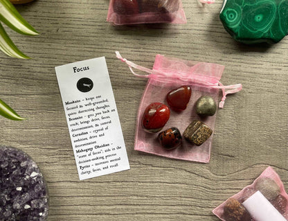 An image of a collection of tumbled stones in an organza bag. To the side is a piece of paper that describes what each tumbled stone's metaphysical properties are. FOCUS Tumbled Crystal Bag