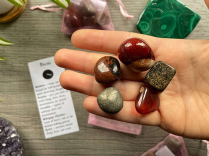 An image of a collection of tumbled stones in an organza bag. To the side is a piece of paper that describes what each tumbled stone's metaphysical properties are. FOCUS Tumbled Crystal Bag close up