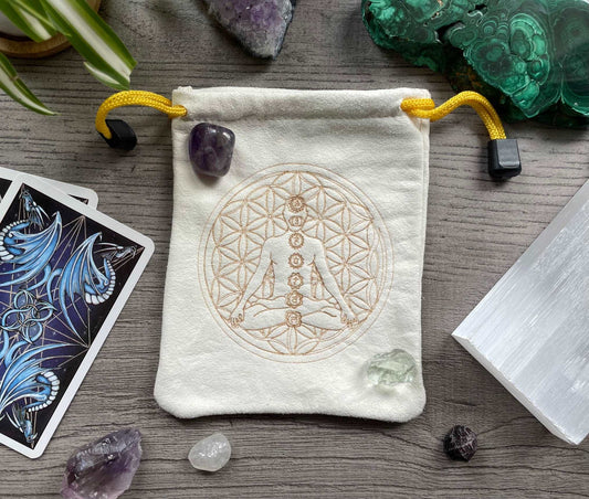 Pictured is a cream-coloured, faux-suede drawstring bag with a flower of life and a meditating person with labelled chakras printed on the front. Flower of Life with Chakras Drawstring Bag