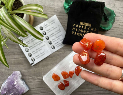 Pictured is a rune set made of carnelian tumbled stones. A black velvet bag and instructions sit nearby, Carnelian Mini Rune Set (24 runes)