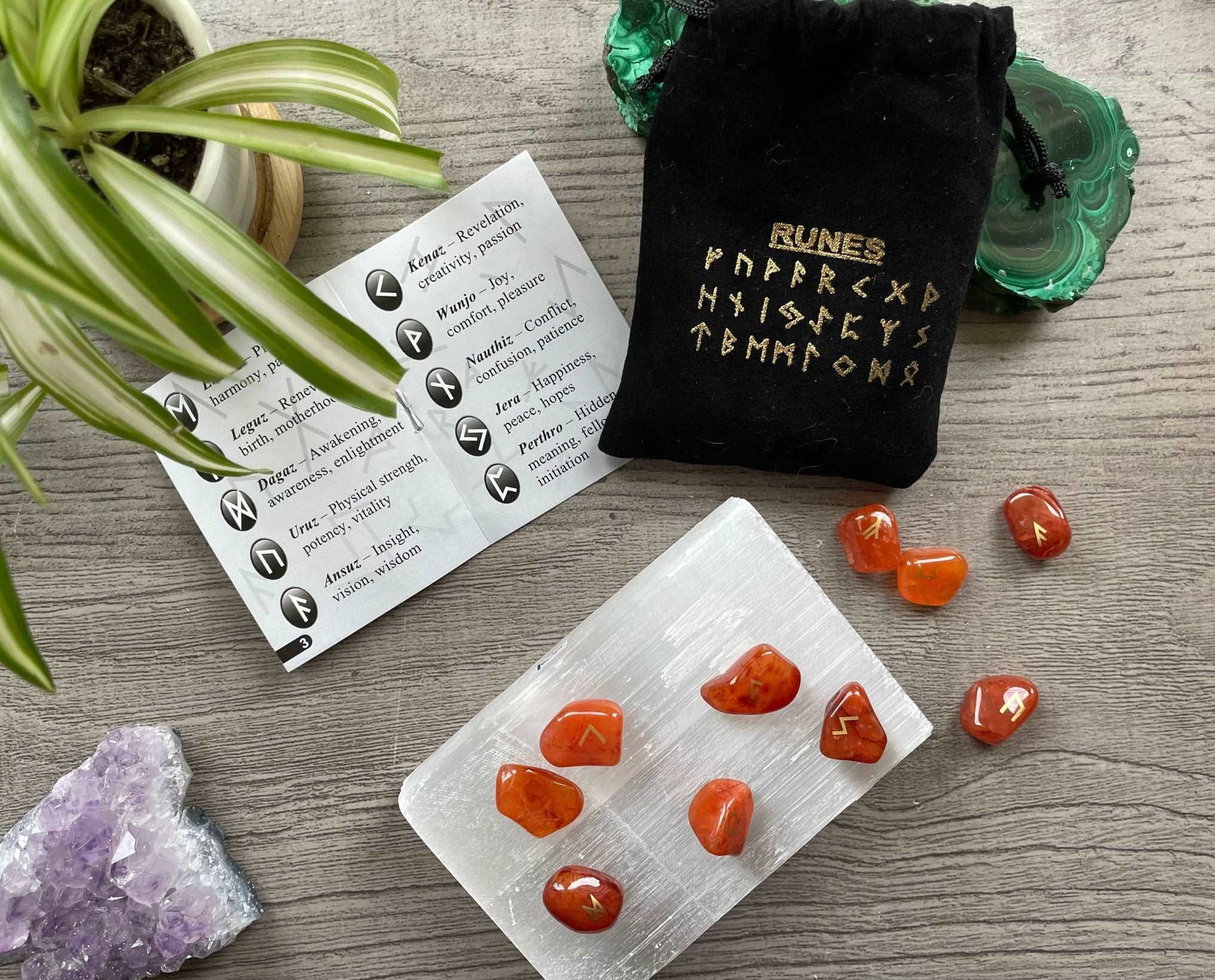 Pictured is a rune set made of carnelian tumbled stones. A black velvet bag and instructions sit nearby, Carnelian Mini Rune Set (24 runes) close up