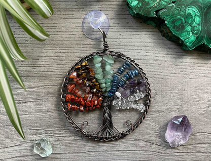 An image of a window art piece with a suction cup. The art is a wire-wrapped tree of life and the leaves on the tree are polished chips of green aventurine, red jasper, carnelian, tiger's eye, aquamarine, amethyst, and clear quartz. Chakra Crystal Gemstones Wire-Wrapped Tree of Life Window Decoration