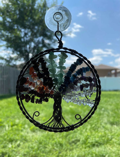 An image of a window art piece with a suction cup. The art is a wire-wrapped tree of life and the leaves on the tree are polished chips of green aventurine, red jasper, carnelian, tiger's eye, aquamarine, amethyst, and clear quartz. Chakra Crystal Gemstones Wire-Wrapped Tree of Life Window Decoration window