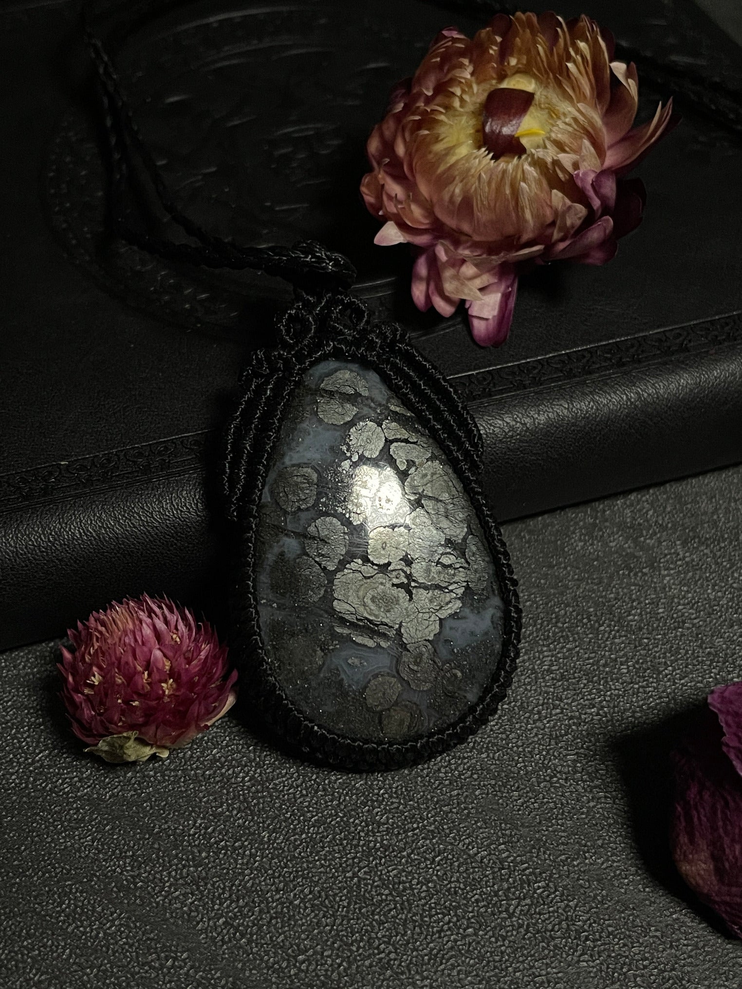 Pictured is a marcasite in agate cabochon wrapped in macrame thread. A gothic book and flowers are nearby. Marcasite in Agate Macramé Necklace (Twisted Nightshade Jewellery) - The Wandering Fox Emporium, Your Crystal Store close up