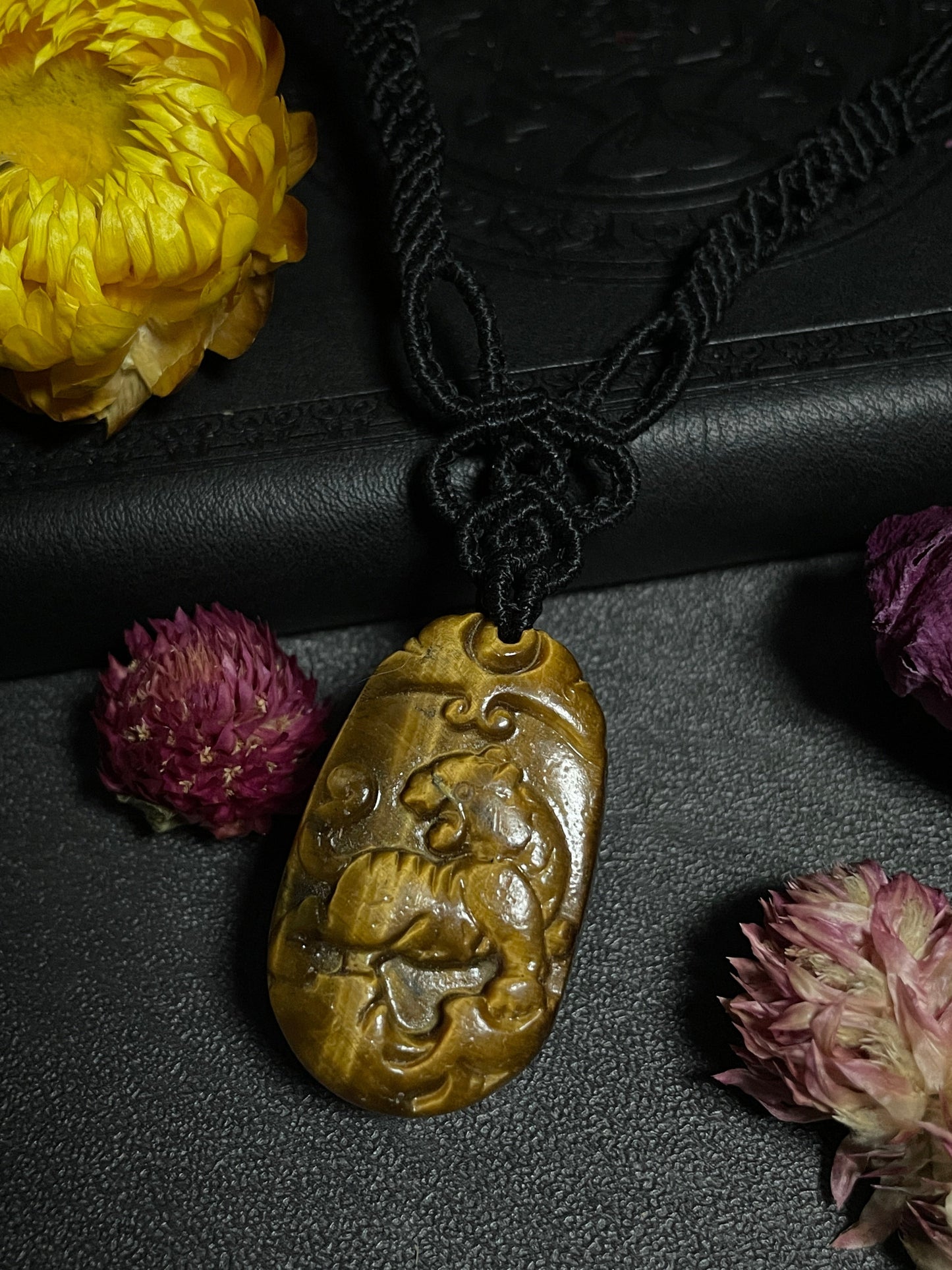 A picture of a tiger pendant carved out of tiger's eye stone. The pendant is on an intricate black macrame necklace. Tiger's Eye Tiger Macramé Necklace (Twisted Nightshade Jewellery) - The Wandering Fox Emporium, Your Crystal Store close up