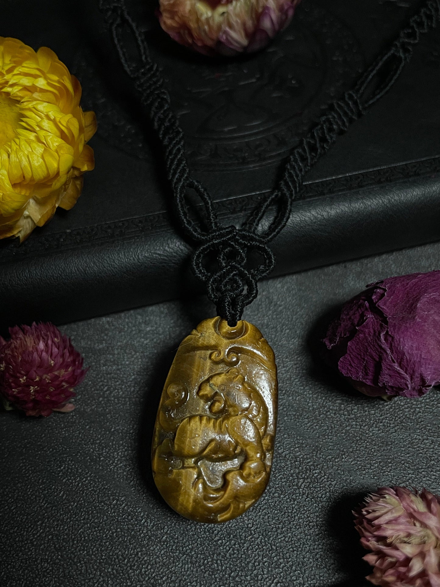 A picture of a tiger pendant carved out of tiger's eye stone. The pendant is on an intricate black macrame necklace. Tiger's Eye Tiger Macramé Necklace (Twisted Nightshade Jewellery) - The Wandering Fox Emporium, Your Crystal Store