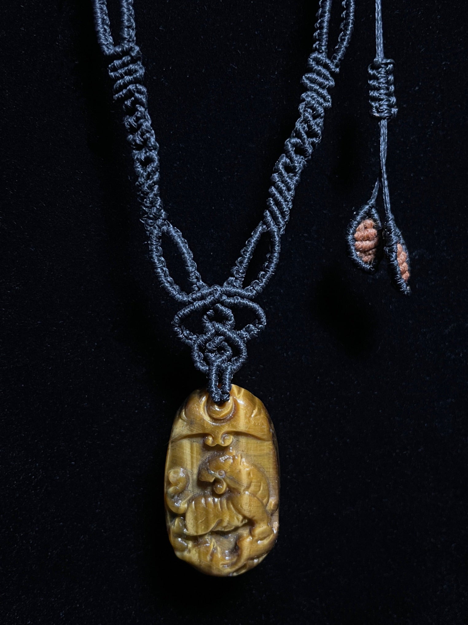 A picture of a tiger pendant carved out of tiger's eye stone. The pendant is on an intricate black macrame necklace. Tiger's Eye Tiger Macramé Necklace (Twisted Nightshade Jewellery) - The Wandering Fox Emporium, Your Crystal Store clasp