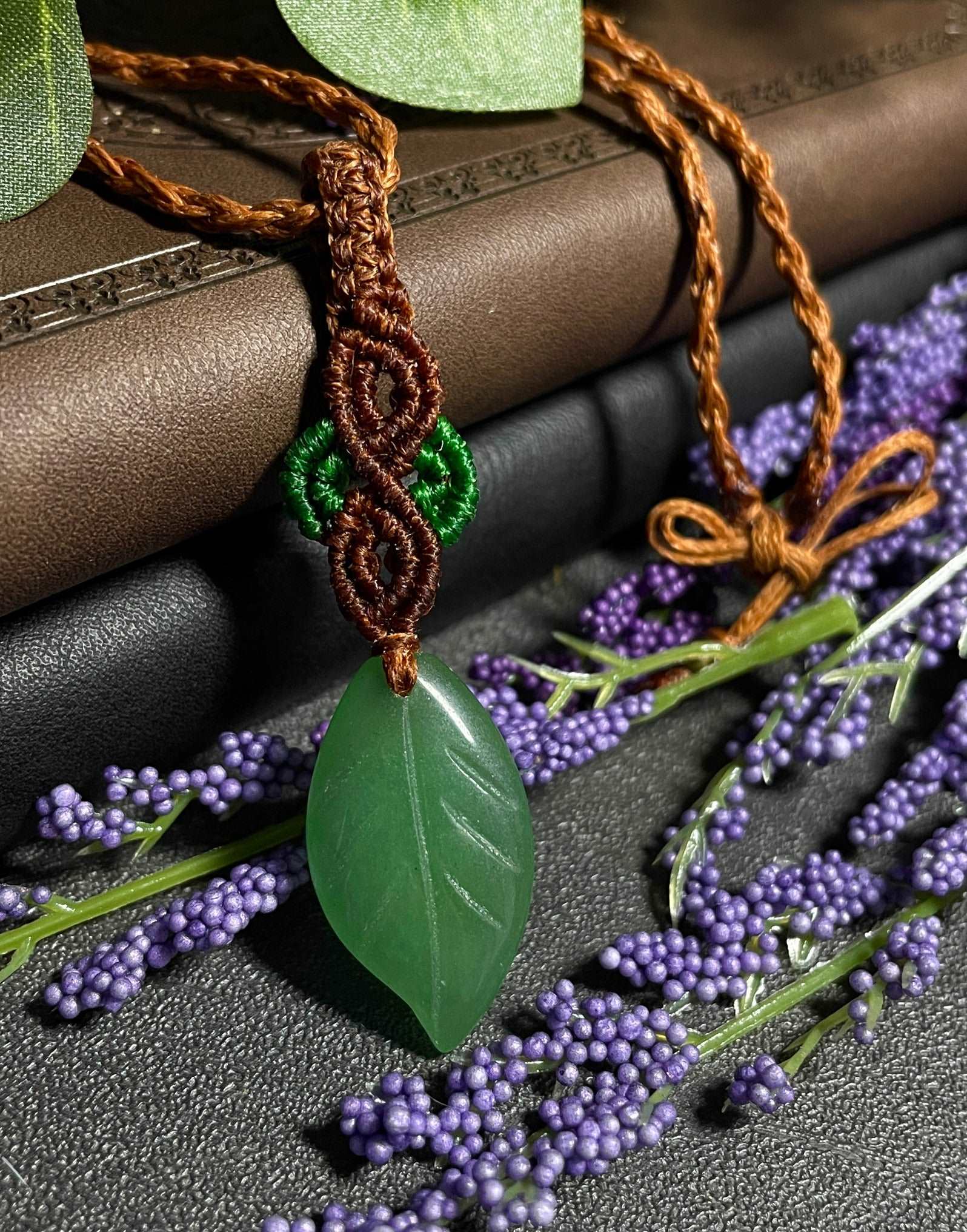 Pictured is a green aventurine cabochon wrapped in macrame thread. A gothic book and flowers are nearby. Green Aventurine Leaf Macramé Necklace (Twisted Nightshade Jewellery) - The Wandering Fox Emporium, Your Crystal Store close up