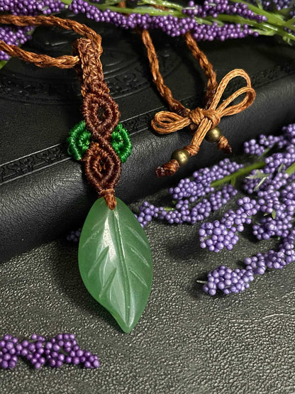 Pictured is a green aventurine cabochon wrapped in macrame thread. A gothic book and flowers are nearby. Green Aventurine Leaf Macramé Necklace (Twisted Nightshade Jewellery) - The Wandering Fox Emporium, Your Crystal Store front