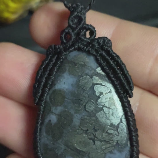 Pictured is a marcasite in agate cabochon wrapped in macrame thread. A gothic book and flowers are nearby. Marcasite in Agate Macramé Necklace (Twisted Nightshade Jewellery) - The Wandering Fox Emporium, Your Crystal Store video