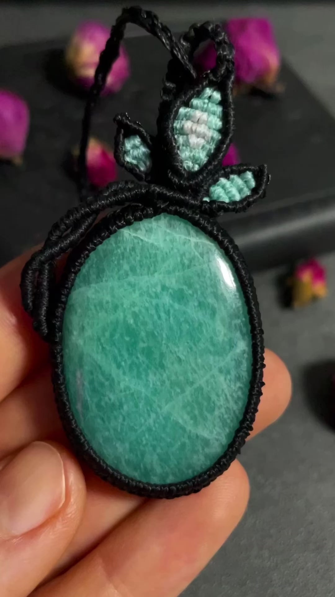 Pictured is an amazonite cabochon wrapped in macrame thread. A gothic book and flowers are nearby. Amazonite Macramé Necklace (Twisted Nightshade Jewellery) - The Wandering Fox Emporium, Your Crystal Store video