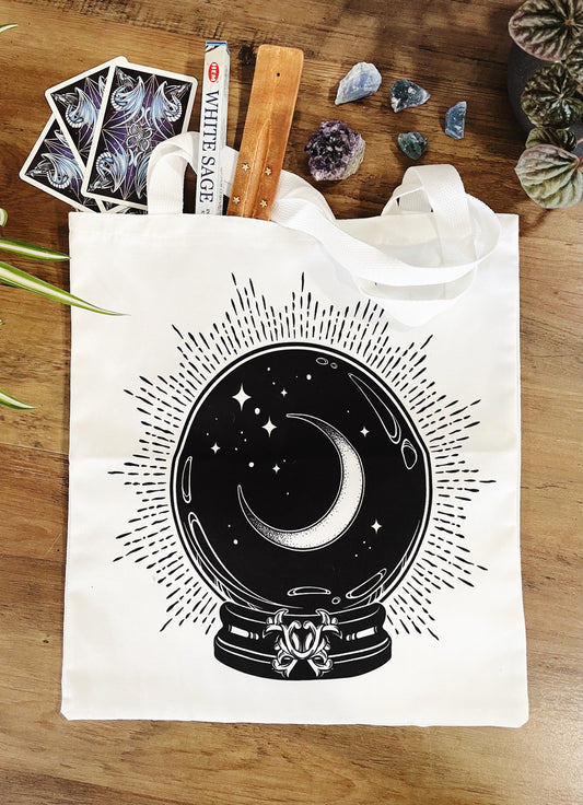 Pictured is a large canvas tote bag featuring an image of a crystal ball with a crescent moon inside. White Crystal Ball Tote Bag