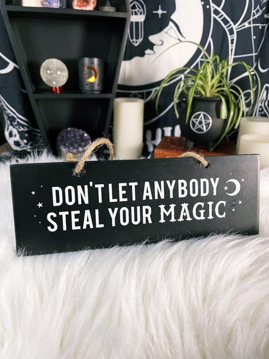 An image of a black sign with white letters that reads "Don't Let Anybody Steal Your Magic." The sign is rectangular and has a thick rope hanger attached to it, making it suitable for hanging on a wall or door.  "Don't Let Anybody Steal Your Magic" Wall Sign