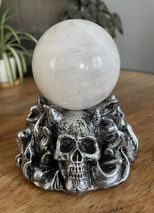 Pictured is a silver resin sphere holder with various demon skulls on it. Horned Demon Skulls Crystal Sphere Stand