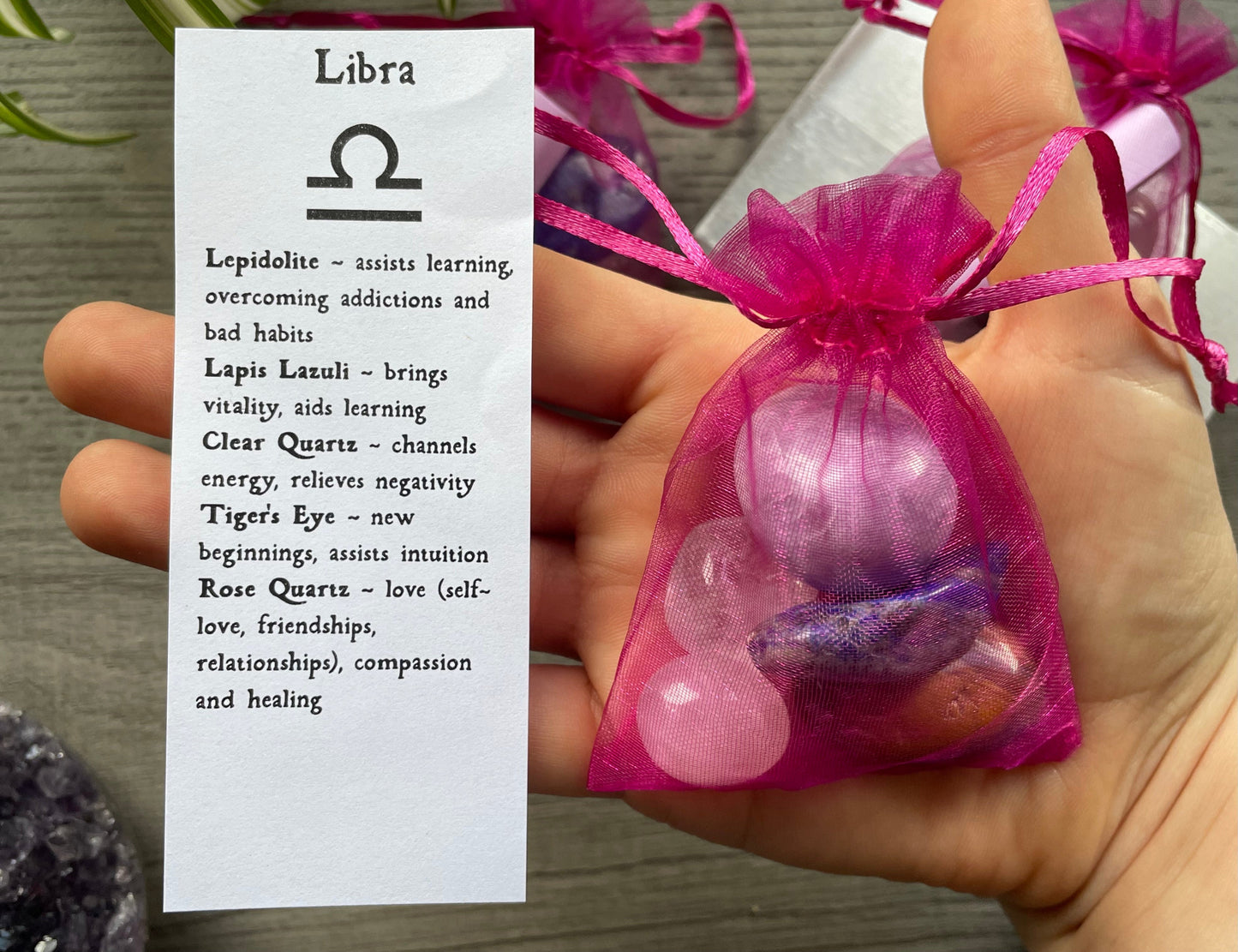 An image of a collection of tumbled stones in an organza bag. To the side is a piece of paper that describes what each tumbled stone's metaphysical properties are. LIBRA Zodiac Tumbled Crystal Bag front