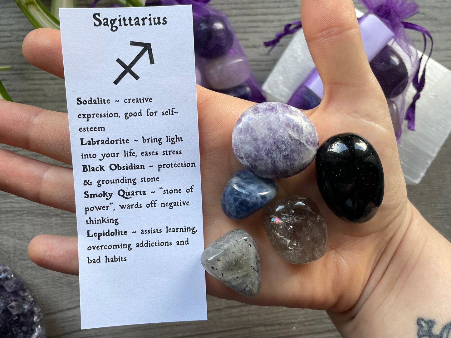 An image of a collection of tumbled stones in an organza bag. To the side is a piece of paper that describes what each tumbled stone's metaphysical properties are. SAGITTARIUS Zodiac Tumbled Crystal Bag crystals