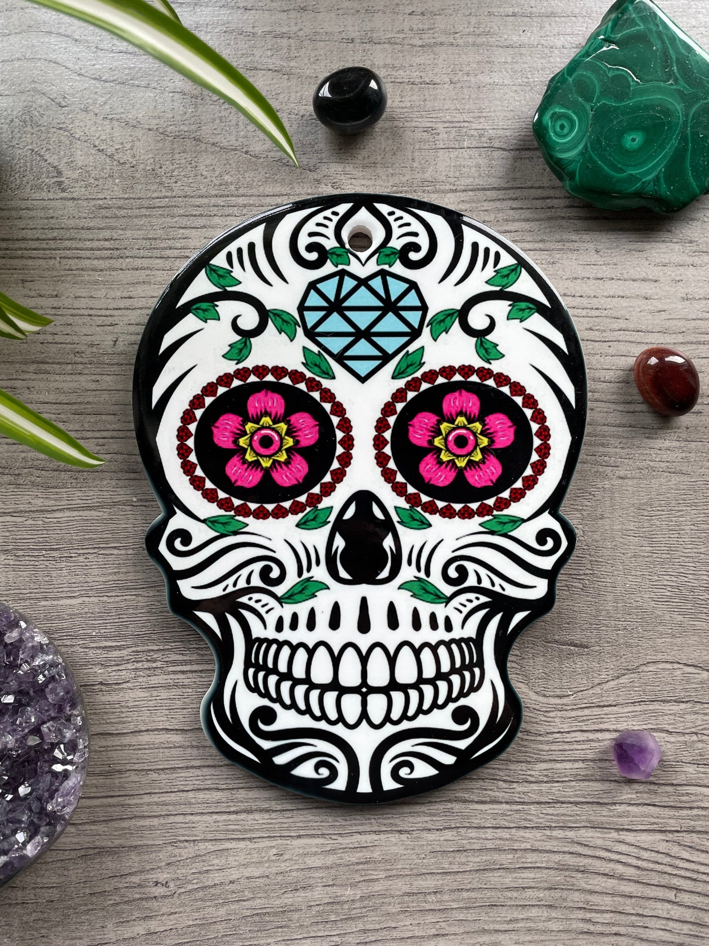 Pictured is a ceramic trivet in the shape of a sugar skull with bright colours. Sugar Skull Ceramic Trivet (B) front