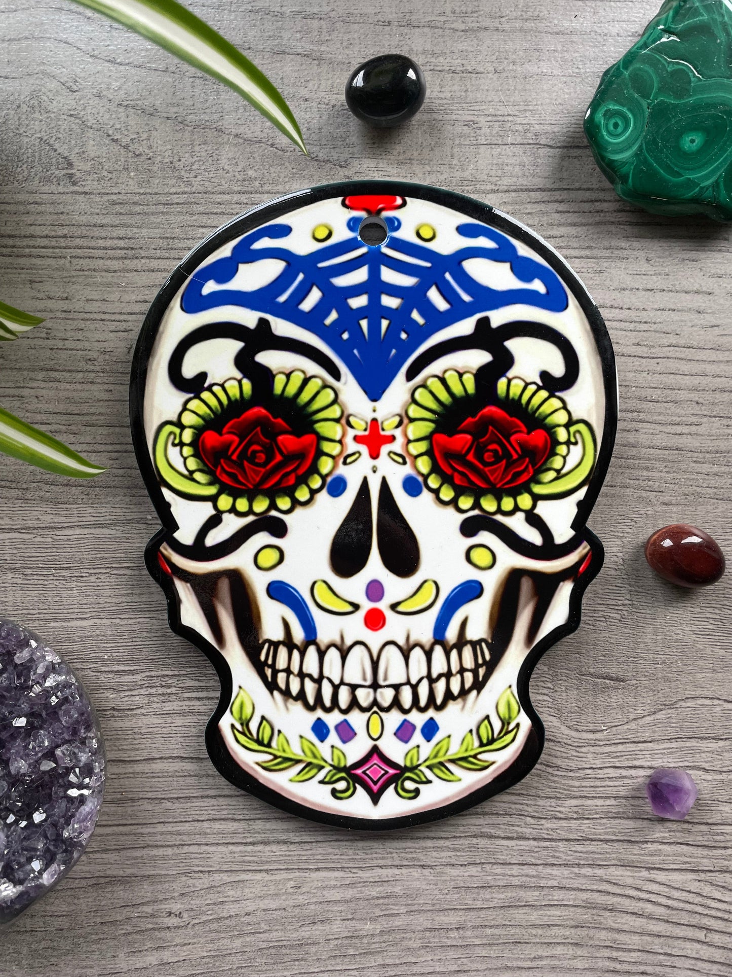 Pictured is a ceramic trivet in the shape of a sugar skull with bright colours. Sugar Skull Ceramic Trivet (A) front