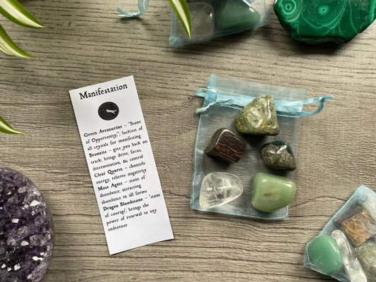 An image of a collection of tumbled stones in an organza bag. To the side is a piece of paper that describes what each tumbled stone's metaphysical properties are. MANIFESTATION Tumbled Crystal Bag