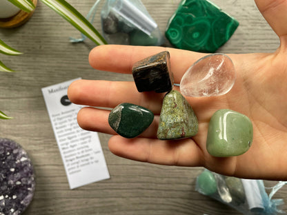 An image of a collection of tumbled stones in an organza bag. To the side is a piece of paper that describes what each tumbled stone's metaphysical properties are. MANIFESTATION Tumbled Crystal Bag close up