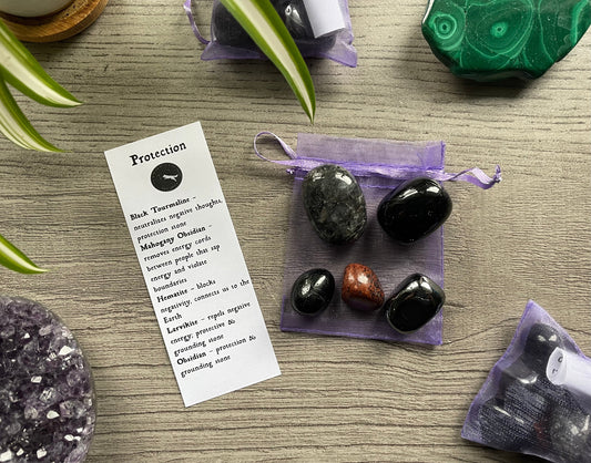 An image of a collection of tumbled stones in an organza bag. To the side is a piece of paper that describes what each tumbled stone's metaphysical properties are. PROTECTION Tumbled Crystal Bag