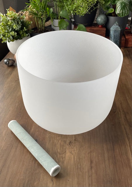  A photo of a quartz crystal singing bowl and a mallet on a wooden surface. The crystal singing bowl is made of clear quartz and has a smooth, round shape. 11" Crystal Singing Bowl (Frosted White) G