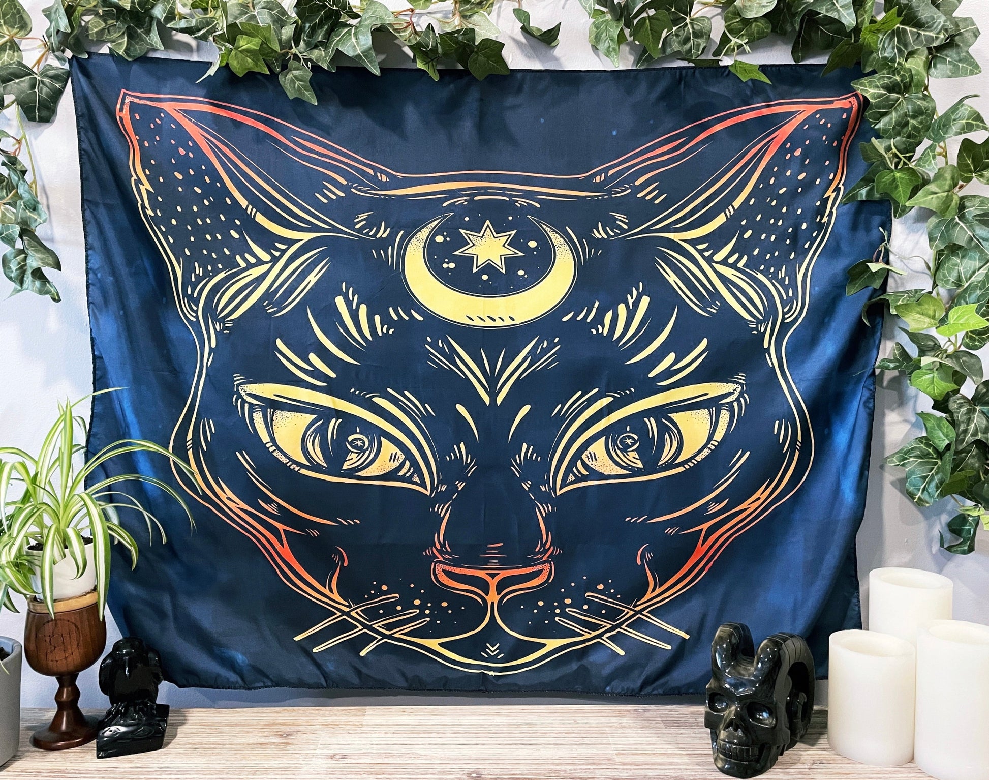 Pictured is a large wall tapestry with a dark blue background and a large cat with a crescent moon on its forehead printed in yellow and orange. Magic Cat Wall Tapestry