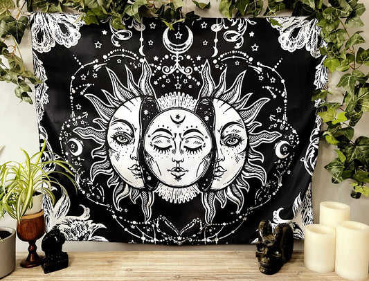 Pictured is a large wall tapestry with a black background and a large moon inside a sun printed in white on it. Moon & Sun Wall Tapestry 