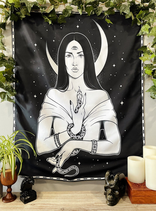 Pictured is a large wall tapestry with a black background and a woman holding a snake with a crescent moon behind her printed in white on it. Third Eye Opening Wall Tapestry 