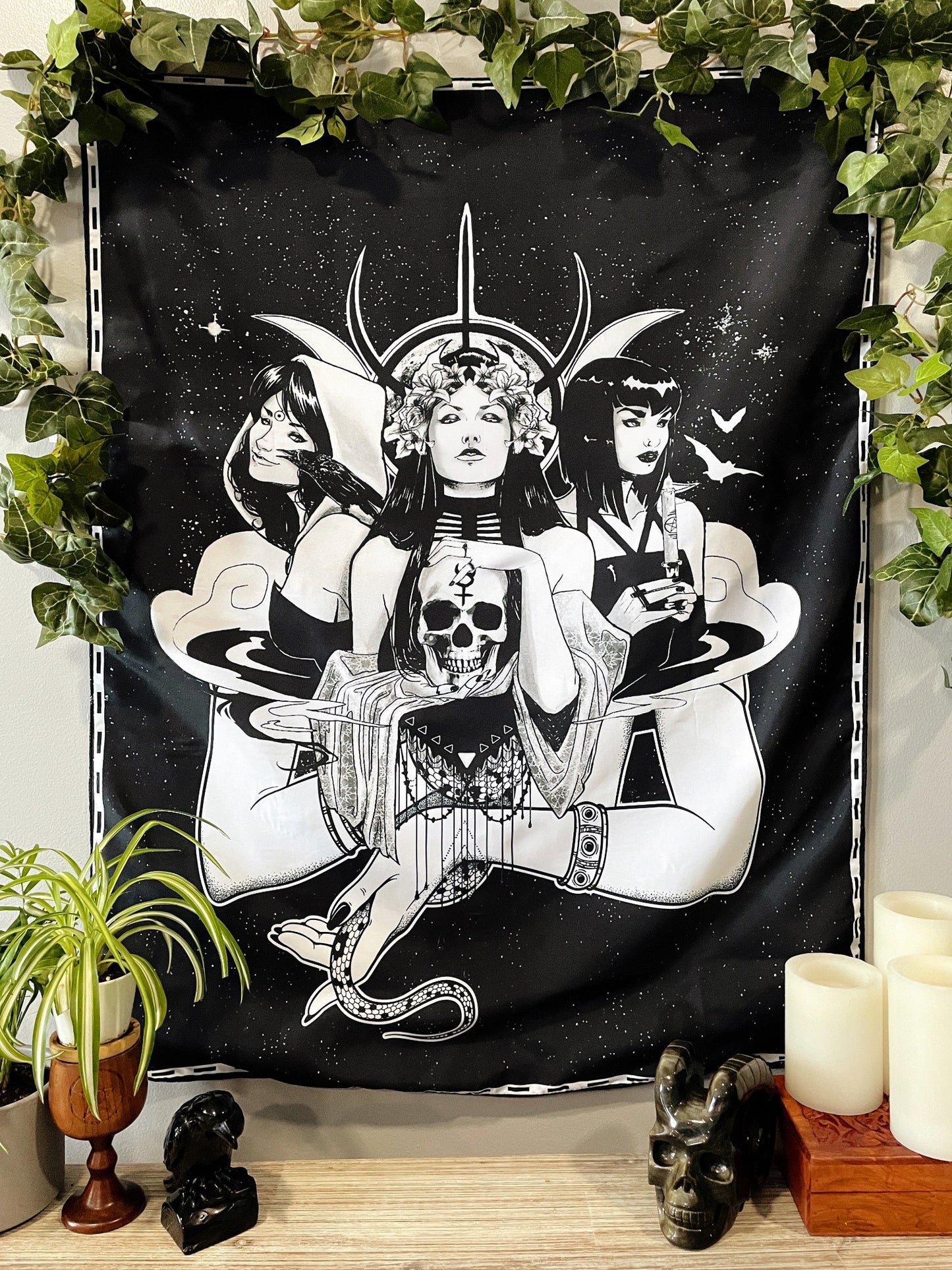 Pictured is a large wall tapestry with a black background and three women representing triple goddesses or Hecate printed in white on it. Triple Moon & Witches Wall Tapestry