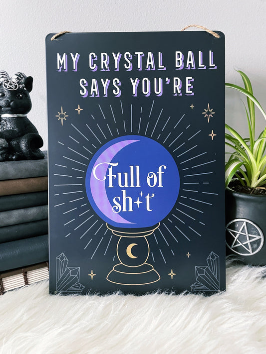 An image of a metal wall sign featuring a crystal ball design with the phrase "My crystal ball says you're full of shit" written in bold letters. The crystal ball design is illustrated in white against a deep purple background, with intricate lines and details that create a mystical and magical look. "My Crystal Ball Says You're Full of Shit" Metal Sign