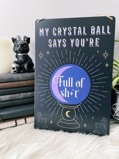 An image of a metal wall sign featuring a crystal ball design with the phrase "My crystal ball says you're full of shit" written in bold letters. The crystal ball design is illustrated in white against a deep purple background, with intricate lines and details that create a mystical and magical look. "My Crystal Ball Says You're Full of Shit" Metal Sign example