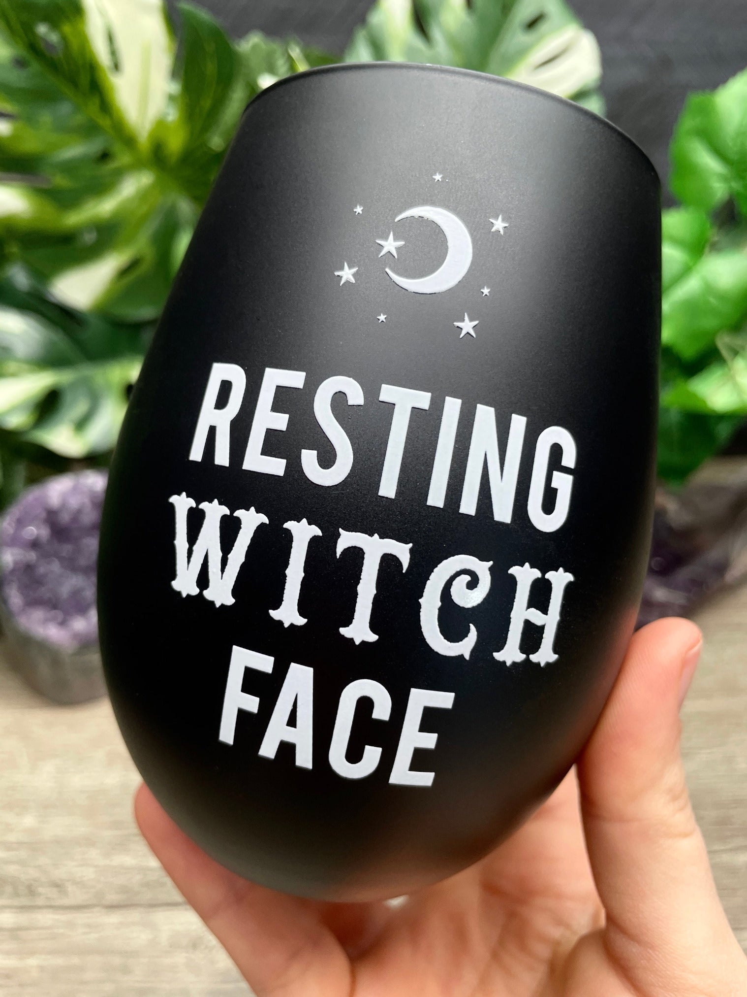 A black stemless wine glass with the words "resting witch face" written on it in white letters. The glass is on a white background. "Resting Witch Face" Stemless Wine Glass close up